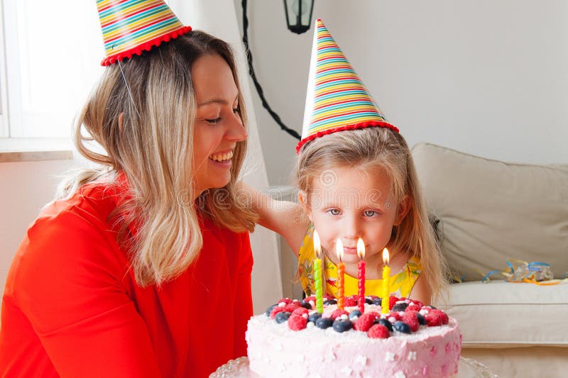 Adorable four years old european blonde girl makes a wish before blowing out the candles on a birthday cake that mom is holding stock photos Adorable four years old european blonde girl makes a wish before blowing out the candles on a birthday cake that mom is holding stock photos