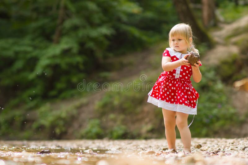 Adorable girl throw stone to river stream in park