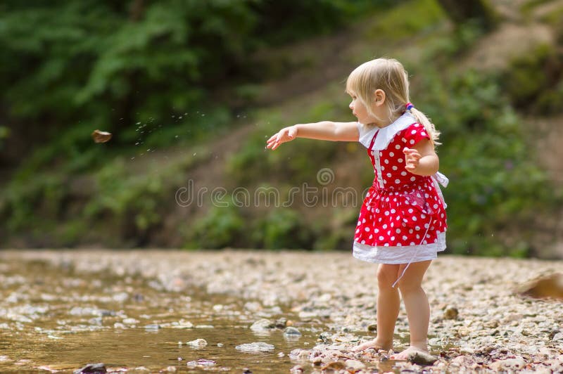 Adorable girl throw stone to river stream in park