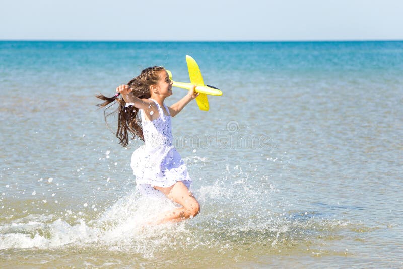 Adorable happy little girl wearing a white dress running through the sea water and playing with the yellow to