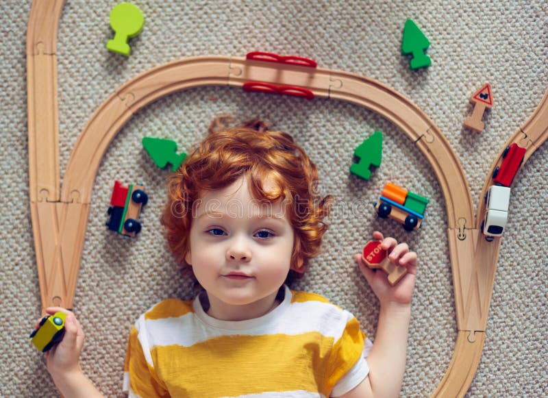 Adorable Happy Rothaarigebaby, das auf den Teppich unter Eisenbahnlinien und Holz Spielzeug der Züge werden stockfotos