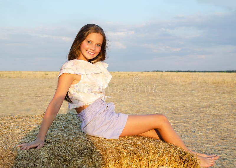 Adorable happy smiling ittle girl child sitting on a hay rolls in a wheat field