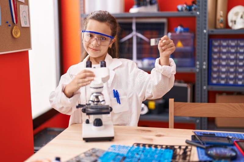 Adorable hispanic girl student using microscope looking sample at classroom stock images