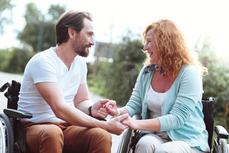 Adorable husband and wife in wheelchairs holding hands together stock photography Adorable husband and wife in wheelchairs holding hands together stock photography