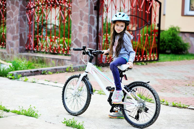 Adorable kid girl in blue helmet riding her bike