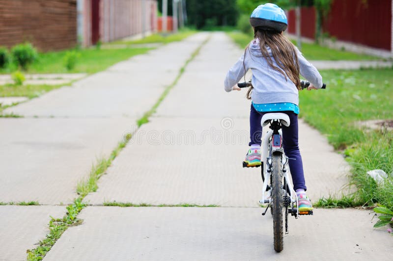 Adorable kid girl in blue helmet riding her bike