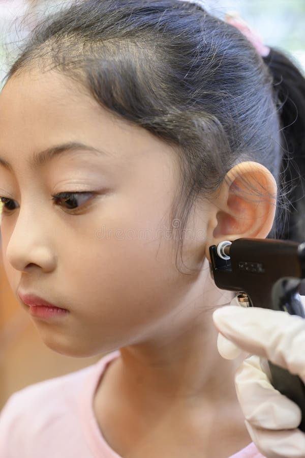 Adorable Little Asian Girl Having Ear Piercing Process. Stock Photo