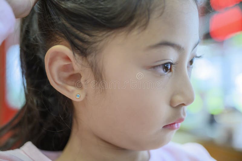 Adorable Little Asian Girl Having Ear Piercing Process. Stock Photo