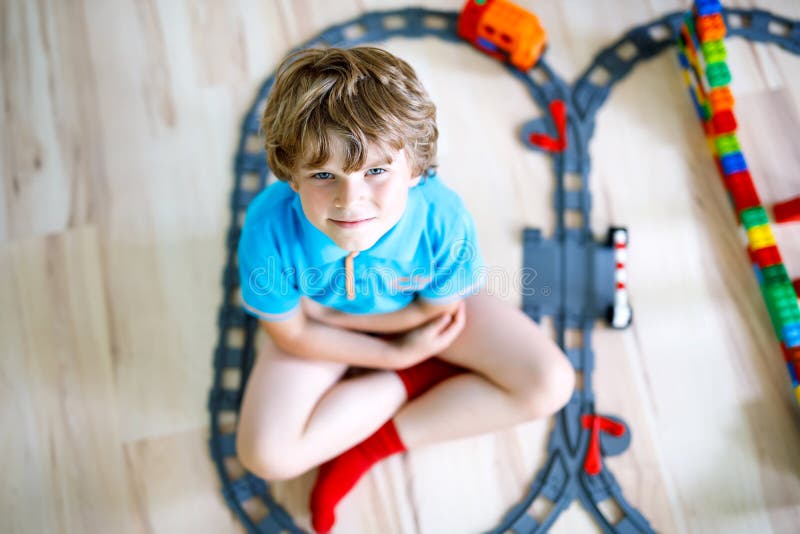 Adorable little blond kid boy playing with colorful plastic blocks and creating train station. Child having fun with stock images Adorable little blond kid boy playing with colorful plastic blocks and creating train station. Child having fun with stock images