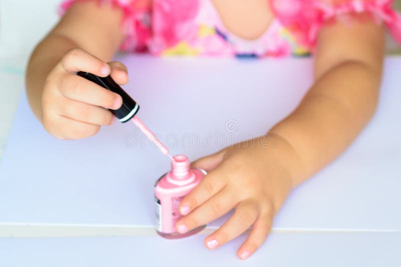 Adorable little girl having fun playing at home with colorful pink nail polish doing manicure and painting nails.