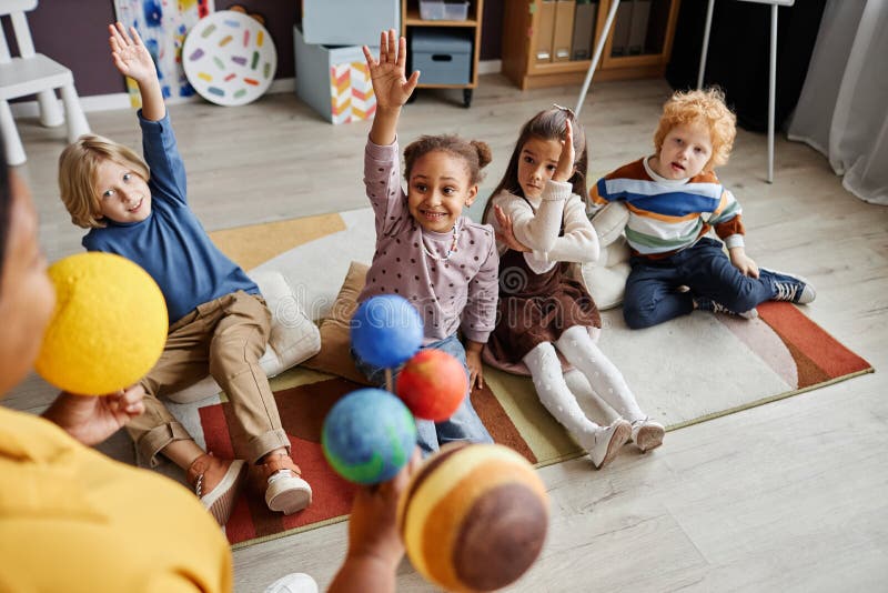 Adorable little girl raising hand while sitting on carpet between classmates royalty free stock photos