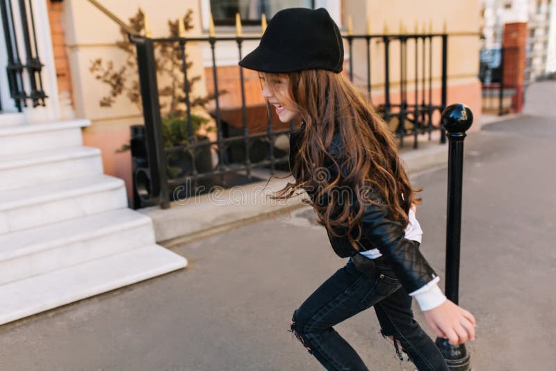 Adorable little girl in trendy black jeans and hat running on the street spending time at fresh air in school vacation royalty free stock photo Adorable little girl in trendy black jeans and hat running on the street spending time at fresh air in school vacation royalty free stock photo