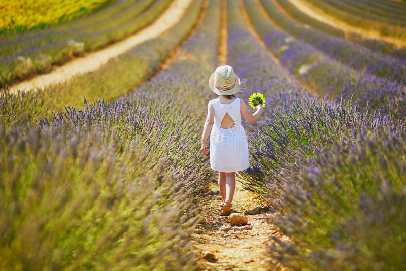 Adorable little girl in white dress and straw hat walking through rows of lavender near Valensole, Provence, France