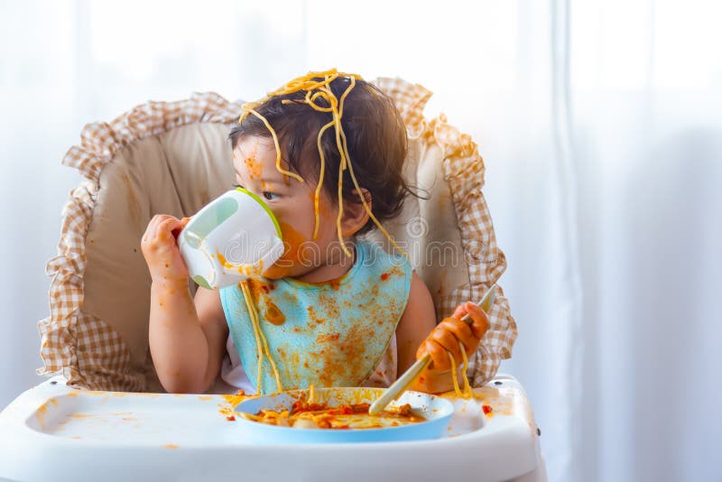 Adorable little toddler girl or infant baby drink water after eat delicious spaghetti food on chair. Funny cute infant girl get