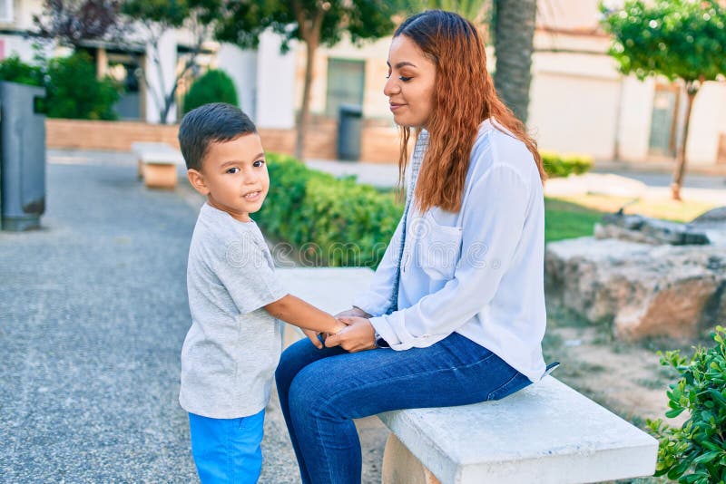 Adorable madre latina e hijo con un gesto encantador sentado en el banco del parque fotos de archivo