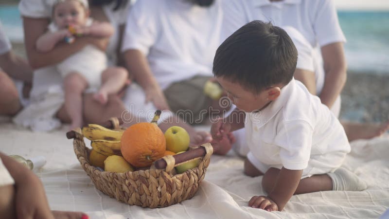 Adorable mignon charmant petit garçon asiatique choisissant des fruits dans le panier avec famille floue reposant à l'arrière-plan