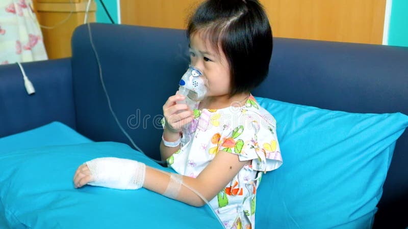 Adorable niño asiático sostiene un inhalador de vapor de máscara para el tratamiento del asma almacen de video