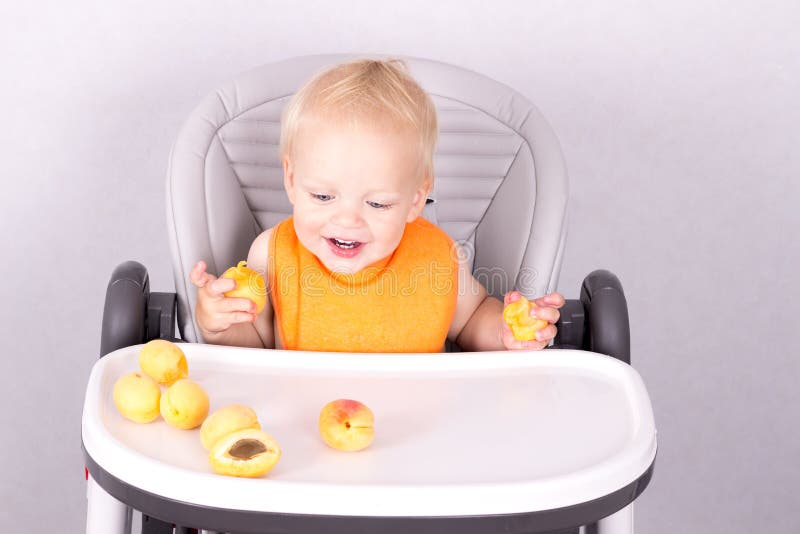 Adorable one year toddler in an orange bip looking at apricots royalty free stock image