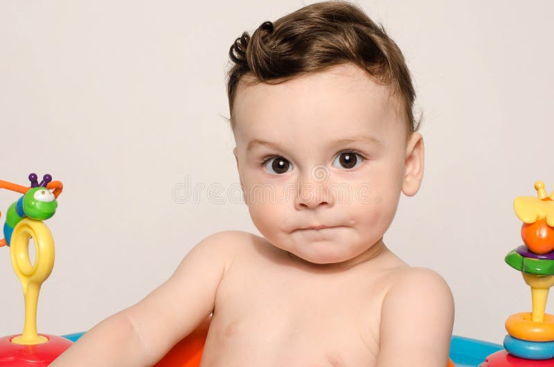 Portrait of a cute baby boy, kid playing with toys, sitiing in a chair stoc...