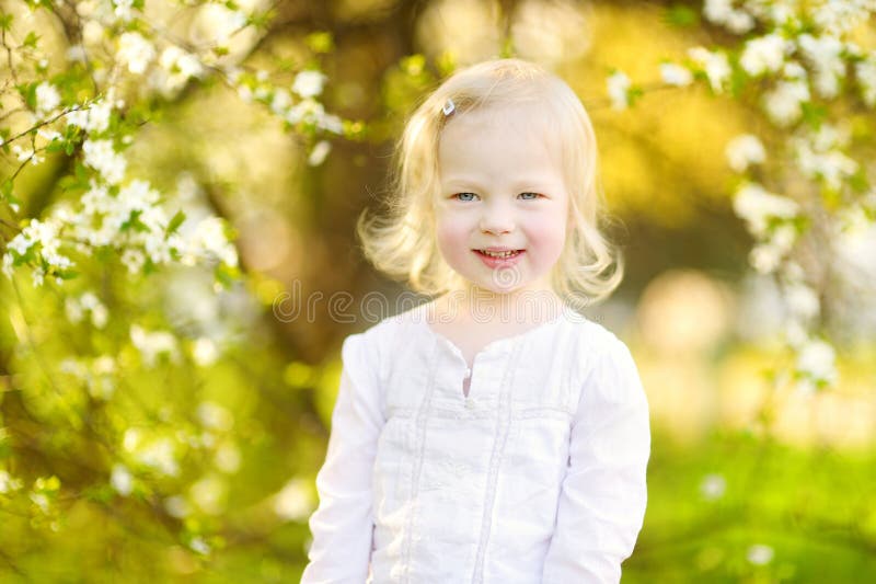 Adorable toddler girl in blooming cherry garden