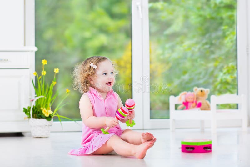 Adorable toddler girl playing maracas in white room