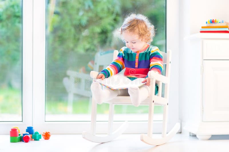 Adorable toddler girl reading book in rocking chair