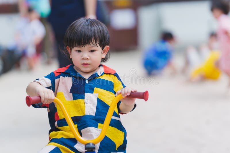 Adorable 2-3 year old Asian boy riding tricycle at playground. Baby was sweating on his face due to hot weather. Child wear colorful clothes. Taking care of the health of young children in the summer.