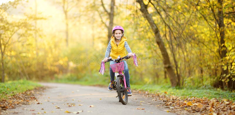 Adorable young girl riding a bike in a city park on sunny autumn day. Active family leisure with kids