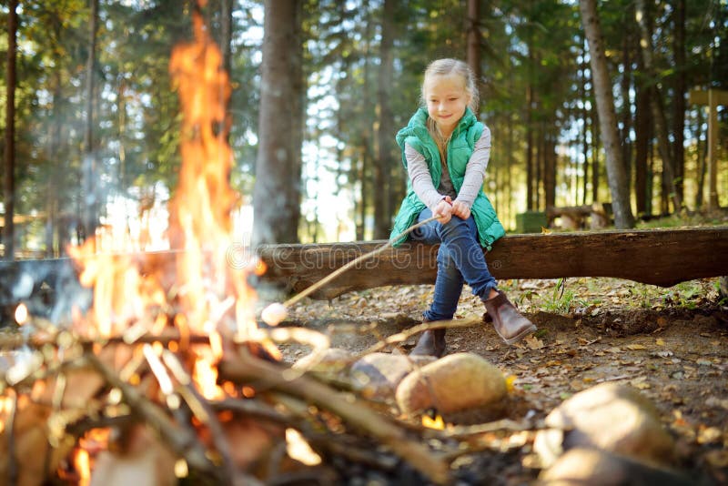Adorable young girl roasting marshmallows on stick at bonfire. Child having fun at camp fire. Camping with children in fall forest royalty free stock images Adorable young girl roasting marshmallows on stick at bonfire. Child having fun at camp fire. Camping with children in fall forest royalty free stock images