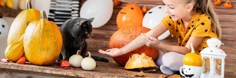 Adorable young girl sitting on a table playing with halloween pumpkin and her pet cat. Halloween lifestyle background. royalty free stock images Adorable young girl sitting on a table playing with halloween pumpkin and her pet cat. Halloween lifestyle background. royalty free stock images