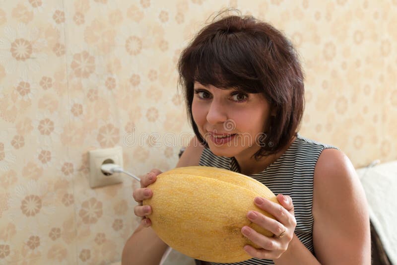 An Adult Brunette Woman Holds A Large Yellow Melon Inhaling Its