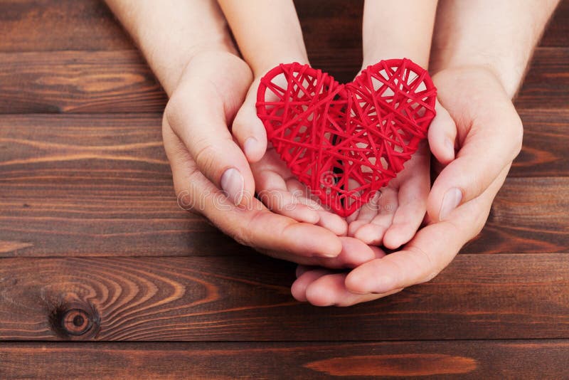 Adult and child holding red heart in hands over a wooden table. Family relationships, health care, pediatric cardiology concept. Adult and child holding red stock images Adult and child holding red heart in hands over a wooden table. Family relationships, health care, pediatric cardiology concept. Adult and child holding red stock images
