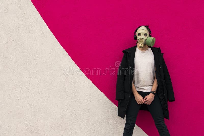 Adult man in gas mask hipster portrait trendy colors photography posing in black coat and white t-shirt on painted vivid pink