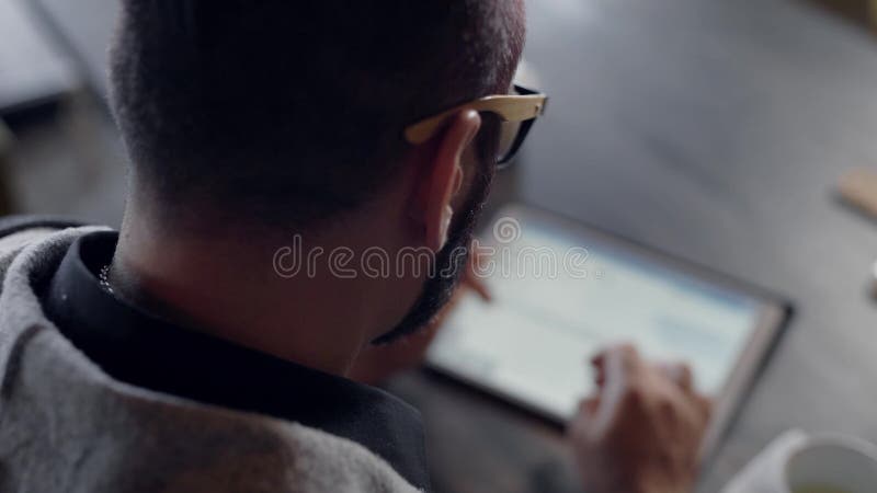 Adult man is working with tablet using wireless internet, browsing sites and typing on touch screen