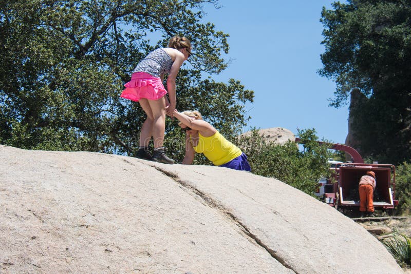 Adult women hikers help each other up on top of a giant boulder. Concept for teamwork, female friendship
