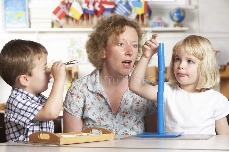 Adulto che aiuta due bambini in giovane età a Montessori/pre fotografie stock libere da diritti Adulto che aiuta due bambini in giovane età a Montessori/pre fotografie stock libere da diritti