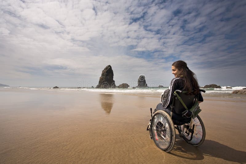 Krásná mladá žena v invalidním vozíku návštěvě Canon Beach v Oregonu, USA.