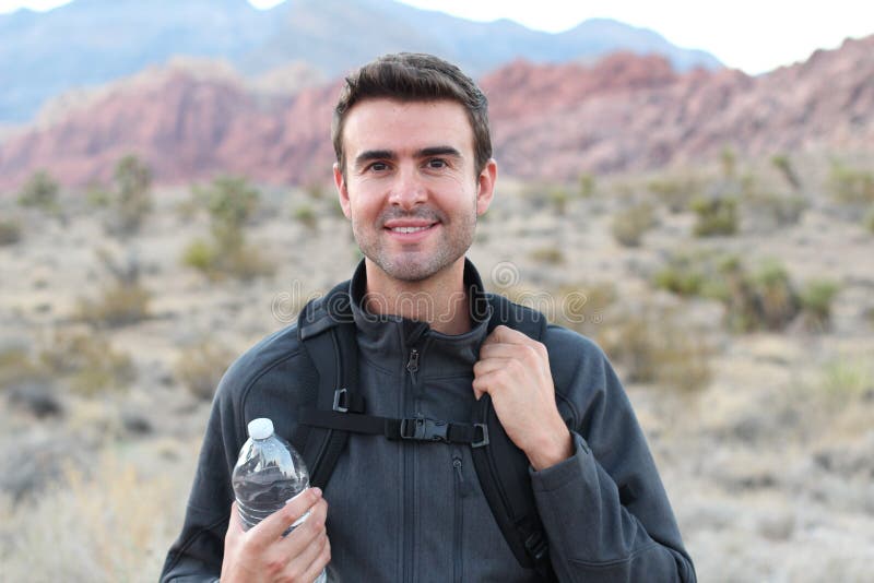 Adventure, travel, tourism, hike and people concept - man holding water bottle and black backpack hiking in the desert
