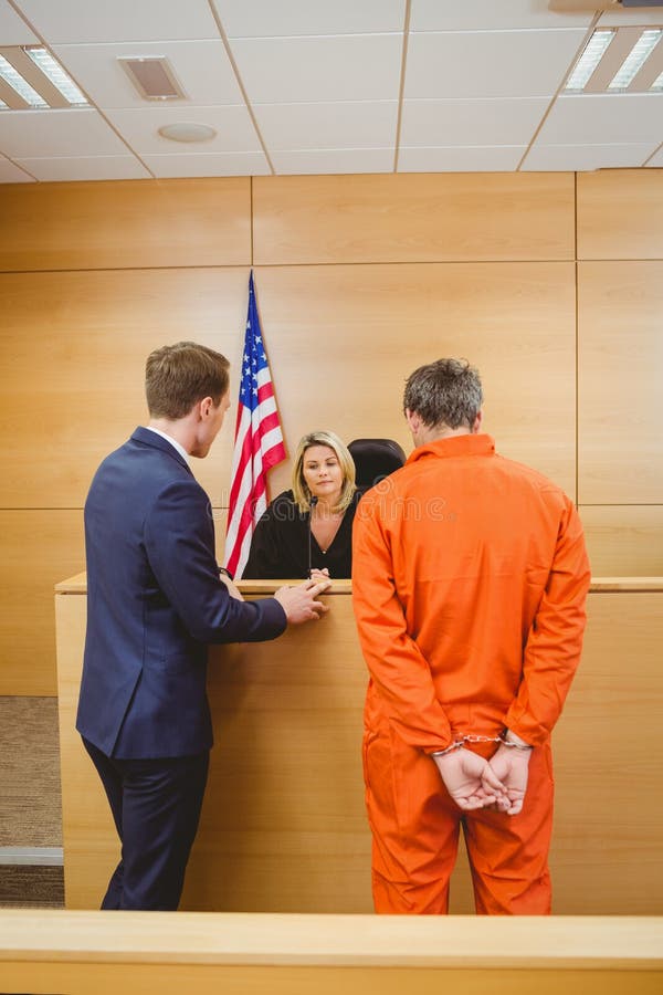 Lawyer and judge speaking next to the criminal in jumpsuit in the court room. Lawyer and judge speaking next to the criminal in jumpsuit in the court room