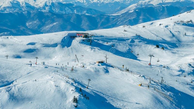 Aerial alpine landscape with snow covered terrain and low clouds drifting above forests and valleys, creating a dramatic winter