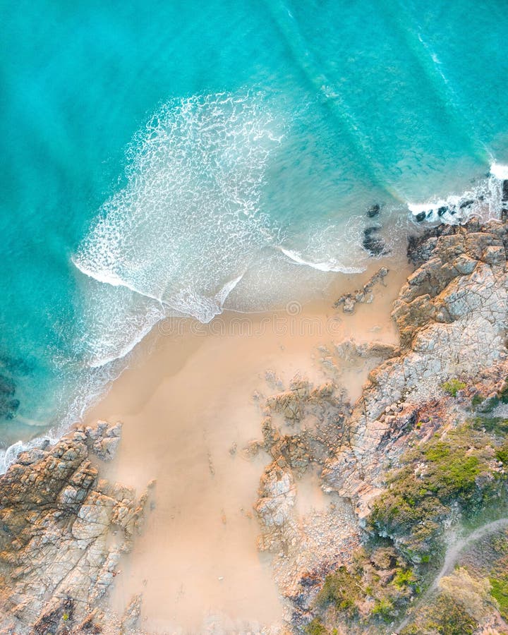 Aerial of a beach with beautiful waves, white sand and rocks at sunset