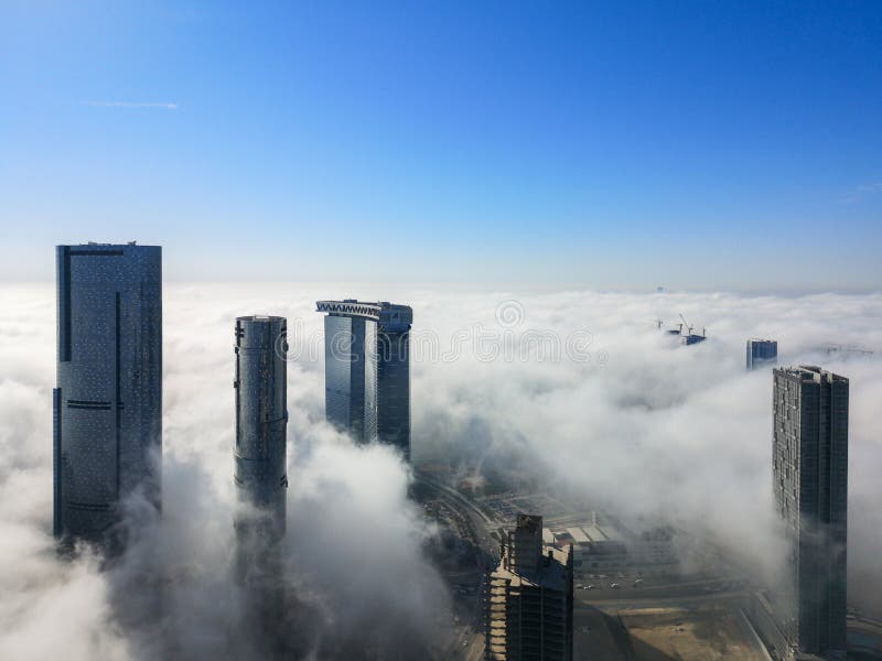 Aerial Drone shot of skyscrapers in the city with fog clouds passing by - Abu Dhabi Al Reem island, Sun, Sky and Gate towers royalty free stock images