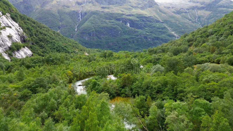 Aerial drone view of a narrow glacial river through a dense green forest in Brenndalsbreen valley stock video footage