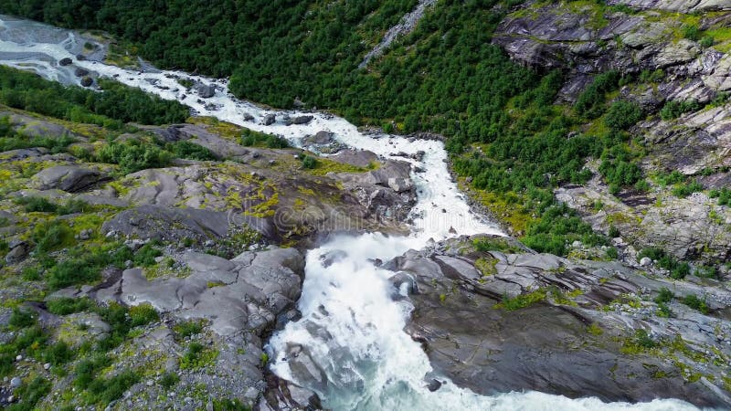 Aerial drone view of a narrow glacial river through a dense green forest in Brenndalsbreen valley stock footage