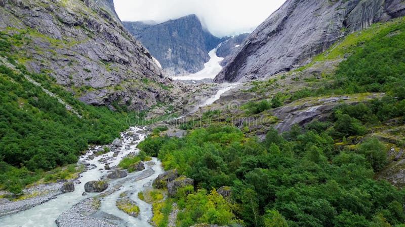 Aerial drone view of a narrow glacial river through a dense green forest in Brenndalsbreen valley stock video