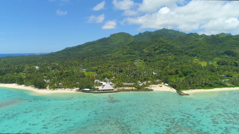 AERIAL: Flying away from green mountainous tropical island and beachfront hotel.