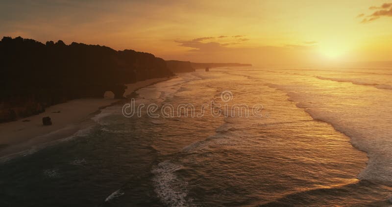 Aerial rolling waves tropical sandy beach at sun set. Slow motion ocean wave. Exotic rocky coast.