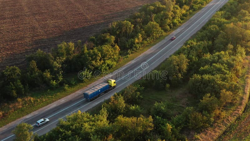 Aerial shot of a grain truck driving on the road in beautiful countryside in the summer sunset. Drone view of lorry