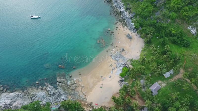 Aerial: small Nui beach with with big stones, blue clear water and green palm trees. Phuket, Thailand. HD