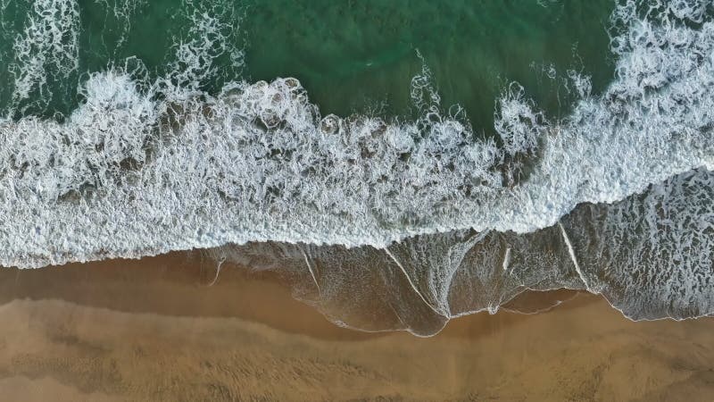 Aerial top down view sandy beach and ocean waves. Sea or ocean waves with white wash. Drone shot of surf with foam and